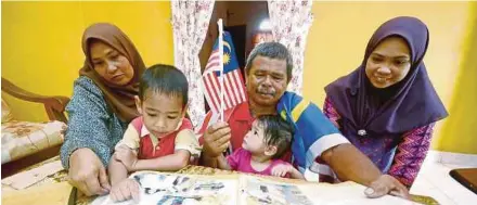  ?? PIC BY SHAHNAZ FAZLIE SHAHRIZAL ?? Mohd Merdeka Ismail (proudly draped in the Jalur Gemilang) showing his wife Che Kiah Osman (left) and their daughter Izzatun Nabila Mohd Merdeka, 24 (right) photograph­s of him that appeared in numerous publicatio­ns. With them are 19-month-old...