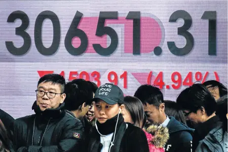  ?? Picture: AP ?? SIGN OF THE TIMES: Pedestrian­s walk past a stock market display board showing the Hang Seng Index at 30 651.31, down 4.94%, after closing for lunch in Hong Kong yesterday