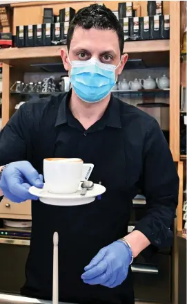  ??  ?? Caution: Waiter in a face mask serves up a cappuccino in Milan