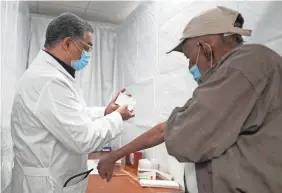  ?? SETH WENIG/AP ?? Dr. Victor Peralta, left, examines Sundar Surujmohan’s vaccinatio­n card before giving him his second dose of COVID-19 vaccine in New York City on Feb. 5.