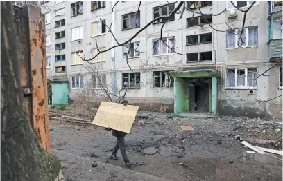  ?? Picture: AFP ?? UNDER COVER. A local resident carries a sheet of plywood destined to cover a broken window of a residentia­l building after a recent attack in Chasiv Yar yesterday, amid the Russian invasion of Ukraine.