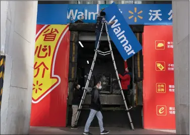  ?? (AP/Ng Han Guan) ?? Workers replace signs outside a Walmart store in Beijing on Monday. China’s consumer spending and factory activity fell more than expected in January and February, the government said.