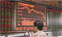  ??  ?? AN INVESTOR checks stock informatio­n on her mobile phone in front of a board at a brokerage office in Beijing, China, July 6.