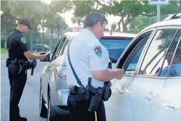  ?? JOE CAVARETTA/SUN SENTINEL ?? Boynton Beach police officers Dennis Castro, left, and Vincent Mastro talk to drivers in a school zone.