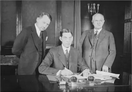  ?? PHOTO LIBRARY OF CONGRESS ?? Secretary of the Interior Ray Lyman Wilbur (center) writing a check for Hoover Dam while flanked by Congressma­n Phil Swing (left) and Sen. Hiram Johnson.