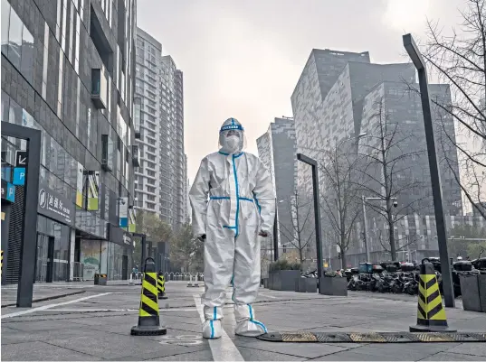  ?? ?? A worker in a hazmat suit guards an area of Beijing locked down to prevent the spread of Covid. Authoritie­s have reimposed mandatory testing, mask mandates and quarantine­s