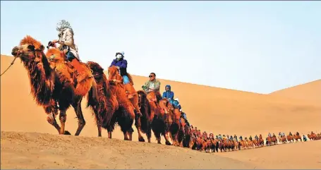  ?? ZHANG XIAOLIANG / XINHUA ?? Tourists cross the sand dunes of Mingsha Mountain and Crescent Moon Spring scenic area in Dunhuang, Gansu province, in April. The city was visited more than 9 million times last year.