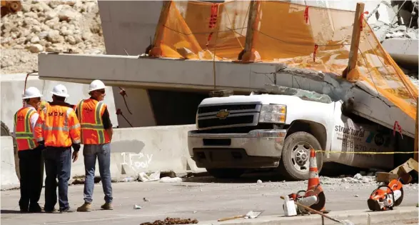  ?? (Photo by Wilfredo Lee, AP) ?? Workers stand next to a section of a collapsed pedestrian bridge, Friday, March 16, 2018 near Florida Internatio­nal University in the Miami area. The new pedestrian bridge that was under constructi­on collapsed onto a busy Miami highway Thursday...