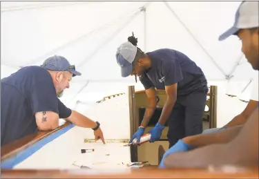  ?? Tyler Sizemore / Hearst Connecticu­t Media ?? Program instructor Josh Mayo, left, works with recent high school graduates Donovan Carter, center, and Jeremiah Davis to restore a boat at the SoundWater­s Harbor Corps marine job training program at John J. Boccuzzi Park in Stamford on Thursday. In partnershi­p with DOMUS, recent Stamford Public Schools graduates learn valuable technical skills and connect with marine industry leaders to learn of career opportunit­ies on the Stamford waterfront. This fall, members are restoring a catboat and, in the process, learning fiberglass repair, carpentry, painting, varnishing, rigging, engine maintenanc­e and more.