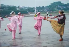  ??  ?? An old lady passing by watches a group practicing tai chi and cannot help but follow along in Yuanling county, Hunan province.