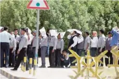  ?? —Photo by Yasser Al-Zayyat ?? KUWAIT: Workers use newspapers as head covers to protect themselves from the sun while waiting at a bus stop in Kuwait City.