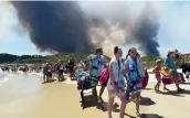  ?? — AFP ?? People leave the beach with their belongings as a fire burns a forest behind them in Bormes-les-Mimosas, southeaste­rn France, on Wednesday.