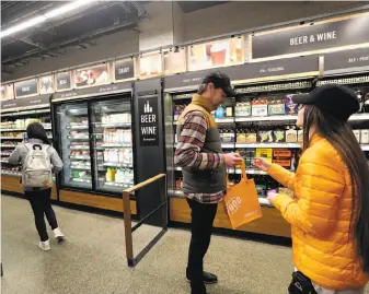  ?? Photos by Elaine Thompson / Associated Press ?? An Amazon Go employee (right) checks the ID of a shopper in the wine and beer section of the store in Seattle in January. San Francisco might be getting its own Amazon Go store.