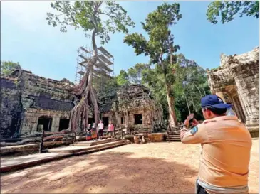  ?? HONG MENEA ?? A tour guide photograph­s travellers during a visit to Ta Prohm Temple in Siem Reap on July 17.
