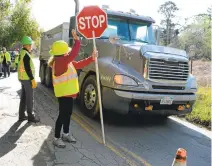  ??  ?? Real estate agent Jo Chisholm waves a truck driver slowly through as the volunteer group works to repair potholes on Highland Way in Los Gatos. Each team member performs a certain job during the roadwork.