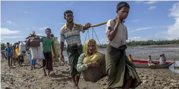  ?? (AP Photo/Dar Yasin) ?? Rohingya Muslims, who crossed over from Myanmar into Bangladesh, carry an elderly woman in a basket and walk towards a refugee camp in Shah Porir Dwip, Bangladesh, Thursday, Sept. 14, 2017. Nearly three weeks into a mass exodus of Rohingya fleeing...