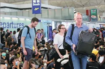  ?? CHINA DAILY ?? Travelers weave their way through protesters at Terminal 1 of Hong Kong Internatio­nal Airport on Monday. Airport Authority Hong Kong canceled Monday’s remaining flights around 4 pm.