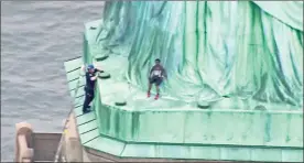  ?? / AP ?? A person, center, leans against the robes of the Statue of Liberty on Liberty Island, as one of the police officers climbed up on a ladder to stand on a ledge nearby talking the climber into descending in New York on Wednesday.