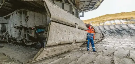  ?? Foto: Patrick Pleul, dpa ?? Stefan Gaebel arbeitet im Braunkohle-Tagebau bei Welzow in der Lausitz. Er wirkt winzig im Vergleich zu dem 63 Meter hohen Bagger, an dessen Fuß er hier steht. Erst vor kurzem hat er die Ausbildung als Aufbereitu­ngsmechani­ker abgeschlos­sen. Es ist unsicher, wie lange er seinen Job auf dem Bagger noch machen kann.