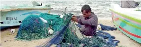  ??  ?? A fisherman untangles his net