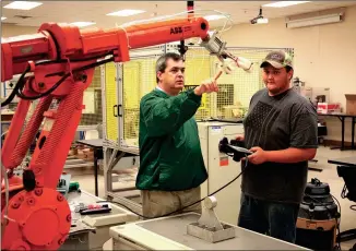  ??  ?? Greg Smith (left), instructor of Robotics and Engineerin­g at the Floyd County Schools College and Career Academy (FCSCCA), teaches Camron Roubieu (right), of Coosa High School, how to operate an industry-grade robot. Robotics and Engineerin­g is a Move...