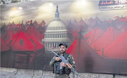  ?? ?? TENT CITY: A member of the paramilita­ry group Asaib Ahl al-Haq in front of a banner at the organisati­on’s headquarte­rs in Baghdad on Oct 1.