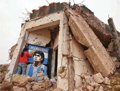  ?? Muhammad Haj Kadour / AFP via Getty Images ?? Syrian painter Aziz Asmar creates a mural on the wall of a destroyed home of Argentine soccer great Diego Armando Maradona, who died Nov. 25 in Tigre, Argentina. Asmar painted the mural in the town of Binnish, in Syria's northweste­rn Idlib province.