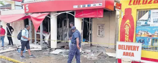  ?? GARETH DAVIS ?? Police personnel and civilians look at the damage caused by the explosion at the Scotiabank ATM in Port Antonio, Portland last Saturday.