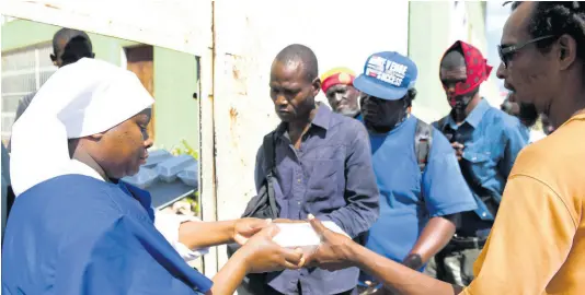  ?? FILE ?? Sister Pauline Rukunyi of Kenya hands out boxed lunches to men waiting on the outside of the Missionari­es of the Poor Sisters’ Holy Innocents Centre at Heroes Circle.