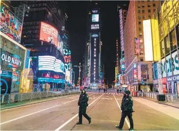  ?? COREY SIPKIN AFP VIA GETTY IMAGES ?? Police officers walk in a nearly empty Times Square due to COVID-19 restrictio­ns on New Year’s Eve.