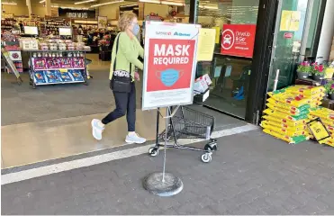  ?? AP Photo/David Zalubowski ?? A shopper pushes her grocery cart past a sign advising the need to wear face masks while in a Safeway grocery store Wednesday in Aurora, Colroado. Retail workers who are fully vaccinated are concerned as retailers loosen mask-wearing restrictio­ns in their establishm­ents.