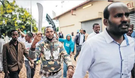  ?? Marco Longari AFP/Getty Images ?? SOMALI migrants carry rocks and a machete in Pretoria, where armed marchers protested the presence of immigrants in the country.