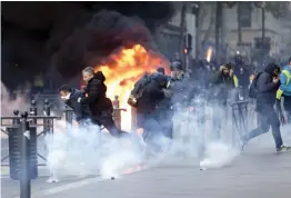  ?? — AP ?? People run away from a burning car during clashes in Marseille, southern France, on Saturday. The grassroots movement began as resistance against a rise in taxes for petrol and diesel, but quickly expanded to encompass frustratio­n at stagnant incomes and the growing cost of living.