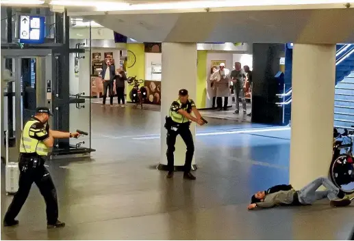  ?? AP ?? Dutch police officers point their guns at a wounded 19-year-old man who was shot by police after stabbing two people in the central railway station in Amsterdam.