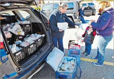  ?? SEAN D. ELLIOT/THE DAY ?? Alexa Dziadul, a food service worker from the Norwich Public Schools, hands Cameron Miller, 6, with his mother, Holly, a bag lunch during a food distributi­on stop at Wequonnoc School on Monday. The district will be distributi­ng food for any child under the age of 18 Monday through Friday for the duration of the shutdown.