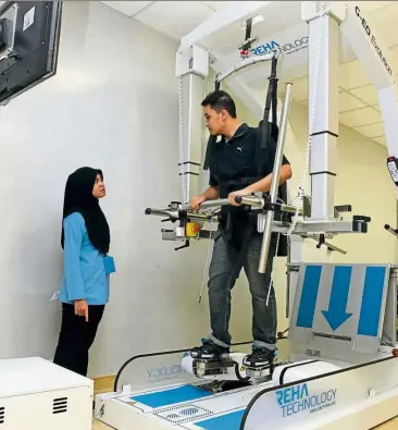  ??  ?? Gullain-Barre Syndrome patient Muhammad Faris Idham (right), 24, talking to a physiother­apist while using the robotic walker machine at the uMMC Rehabilita­tion Medicine Department.