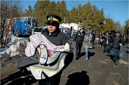  ?? PHOTO: REUTERS ?? A Royal Canadian Mounted Police officer carries a child in a car seat as the mother is escorted to a waiting vehicle after crossing the border from the United States into Hemmingfor­d, Quebec yesterday. A family of four crossed as the RCMP was...