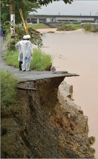 ?? Photo: AFP ?? Local residents look at the damaged river embankment following heavy flooding in Asakura, Fukuoka prefecture, on Thursday. At least two people have been killed and 20 others are missing in huge floods that are surging through southern Japan, with...