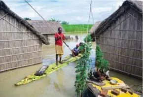  ?? – AFP ?? INUNDATED: A man transports his family past homes submerged in flood waters in Batahidia on the Brahmaputr­a River in South Kamrup, southwest of Guwahati, on Wednesday.