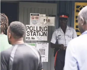  ??  ?? A police officer looks on as voters stand in line at a polling station.