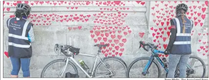  ?? Tony Hicks The Associated Press ?? Women draw hearts, commemorat­ing those who died from COVID-19, on “The National COVID Memorial Wall” on the south bank of the River Thames opposite the House of Parliament in London on Sunday.