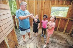  ?? MICHAEL BRYANT PHILADELPH­IA INQUIRER ?? John Collins, left, uses sign language to indicate that there is an insect that could sting, to let the girls, Madeline McHenry, 6, Grace Collins-Alicea, 6, and Rachael Pomroy, 9, know they need to leave the tree house because he found a small wasp nest in the eaves.