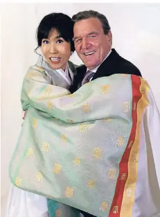  ?? FOTO: DPA ?? Gerhard Schröder und Soyeon Kim, die eine koreanisch­e Tracht trägt, stehen vor einer Fotowand beim festlichen Empfang im Hotel Adlon.