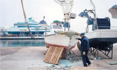  ?? SAMUEL ARANDA/THE NEW YORK TIMES 2021 ?? A man works on a small boat with a luxury yacht looming in the background in Barcelona, Spain.