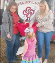  ?? Westside Eagle Observer/SUSAN HOLLAND ?? A pretty young trick-or-treater with a big bow in her hair stops by the Grand Savings Bank Grandyland trunk to select some candy from its big pink bucket. Mandy Carnahan and Jeannette Westrick were working the booth, decorated with several large candies, at Saturday night’s Gravette fall festival trunk or treat event.