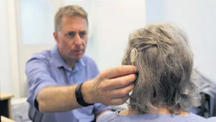  ??  ?? > Consultant clinical scientist (audiology) Dr Hugh Cooper fitting a cochlear implant to a patient at the QE