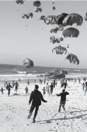  ?? TNS ?? This image from an AFPTV video shows Palestinia­ns running toward parachutes attached to food parcels, after they were air-dropped from U.S. military aircraft on a beach in the Gaza Strip on Saturday.