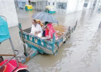  ?? — Reuters ?? People sit in a tractor trolley as they move out of a flooded area after heavy rain in Ahmedabad on Monday.