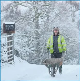  ??  ?? A workman wheels his barrow through the drifts of snow in Daviot, near Inverness