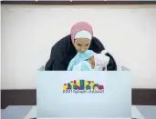  ?? MAJDI MOHAMMED/AP ?? A woman holds a baby as she votes during municipal elections Saturday in the West Bank.